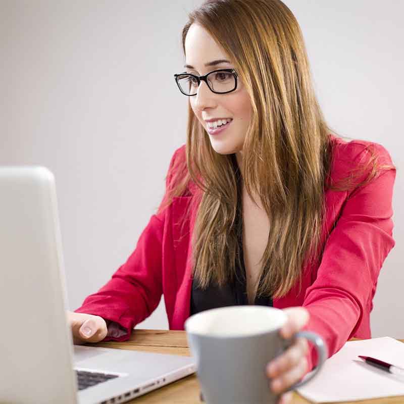 Woman in red jacket looking pleased while using laptop
